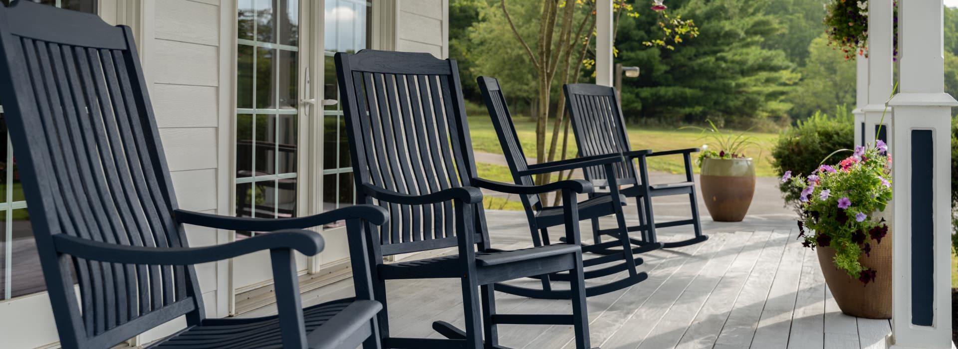 Exterior view of the property's front porch with navy wooden rocking chairs and large pots with colorful flowers