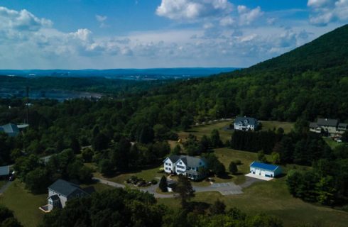 Exterior aerial view of property surrounded by green grass, bushes and trees