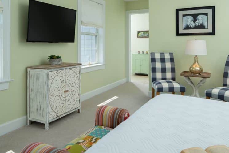 Bedroom with light green walls, carpeting, white bedding, sitting area, wooden cabinet, and wall-mounted TV