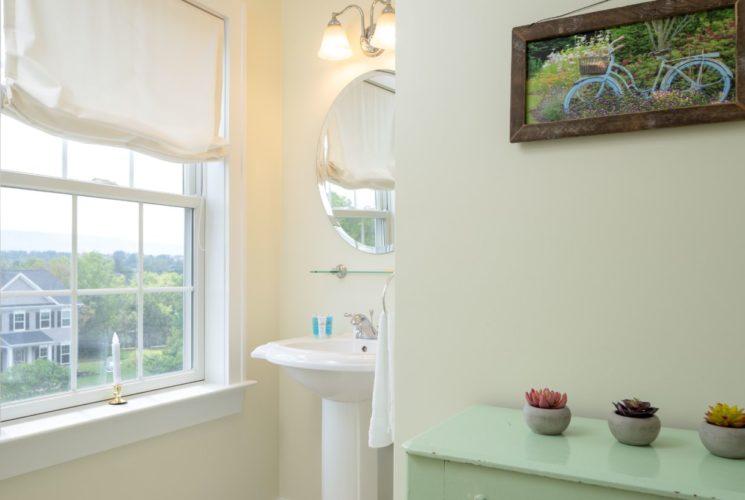 Bathroom with light cream walls, white trim, white pedestal sink, oval mirror, and window to the outside