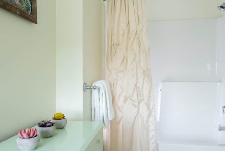 Bathroom with light cream walls, light green dresser, and white tub with shower