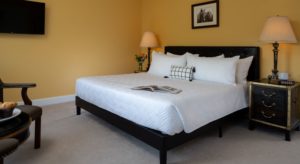 Bedroom with light orange walls, carpeting, black upholstered bed, white bedding, ornate nightstands with lamps, sitting area, and wall-mounted TV