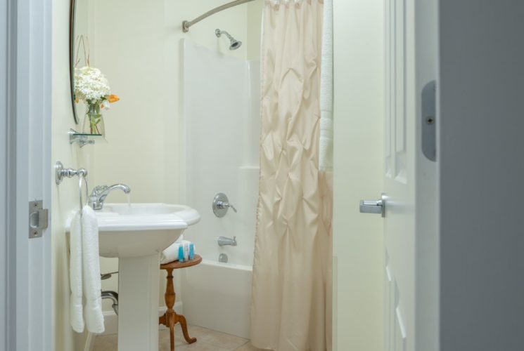 Bathroom with light yellow walls, white pedestal sink, and white tub with shower