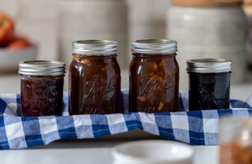Four glass jars filled with different preserves sitting on a blue and white checked towel in a small tray