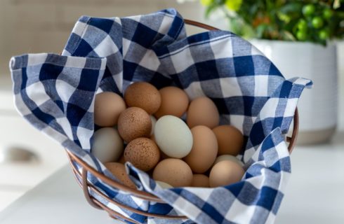 Copper wire basket lined with a blue and white checked towel filled with farm-fresh brown and white eggs