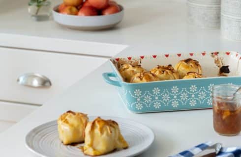 Close up view of apple dumplings in a light blue casserole dish and white plate on white counter