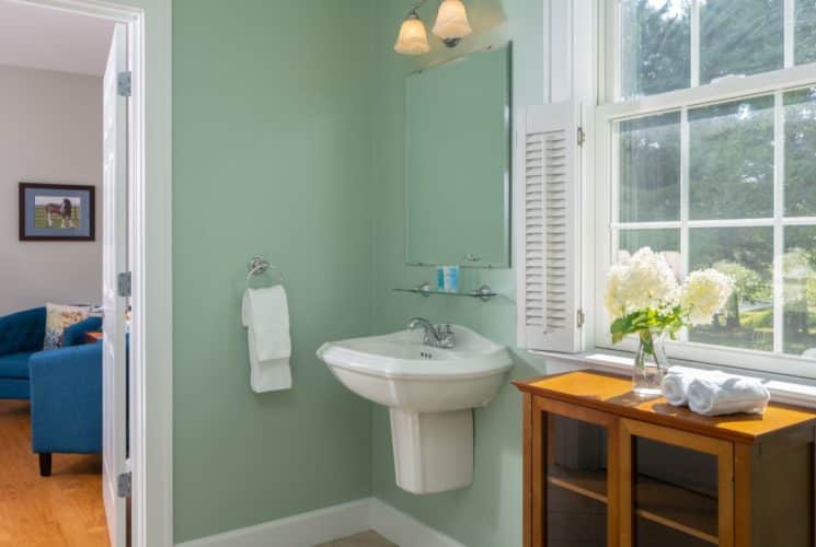 Bathroom with white floating white sink, small mirror, wooden cabinet, and view into the bedroom