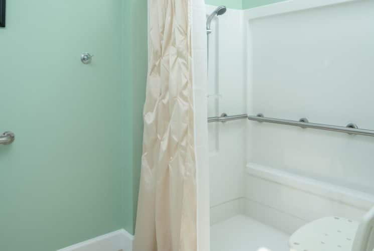 Bathroom with light green walls, roll-in shower, seat, and grab bars