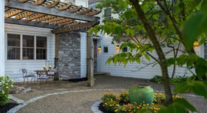 Exterior view of the property's patio covered by a wooden pergola next to gravel path and orange flowers and trees