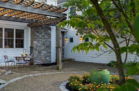 Exterior view of the property's patio covered by a wooden pergola next to gravel path and orange flowers and trees