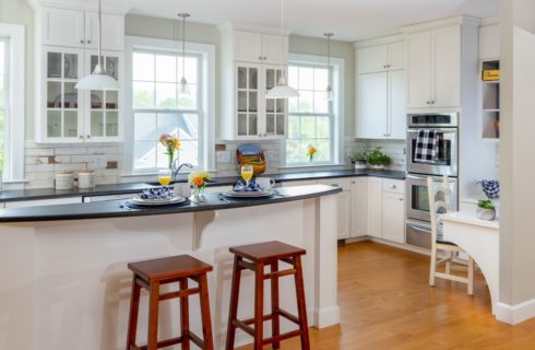 Large kitchen with white cabinets, dark countertop, island, wooden barstools, stainless steel appliances, and multiple windows