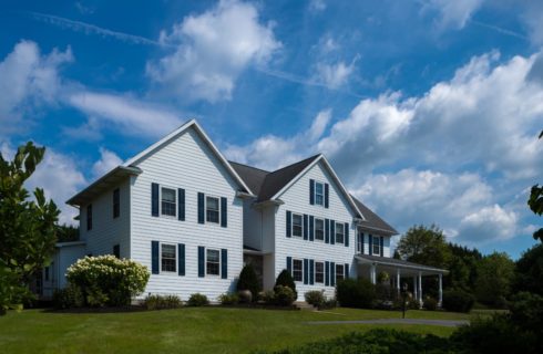 Exterior view of the property painted white with navy shutters and surrounded by green grass, bushes, and trees