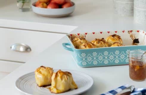 Close up view of apple dumplings in a light blue casserole dish and white plate on white counter