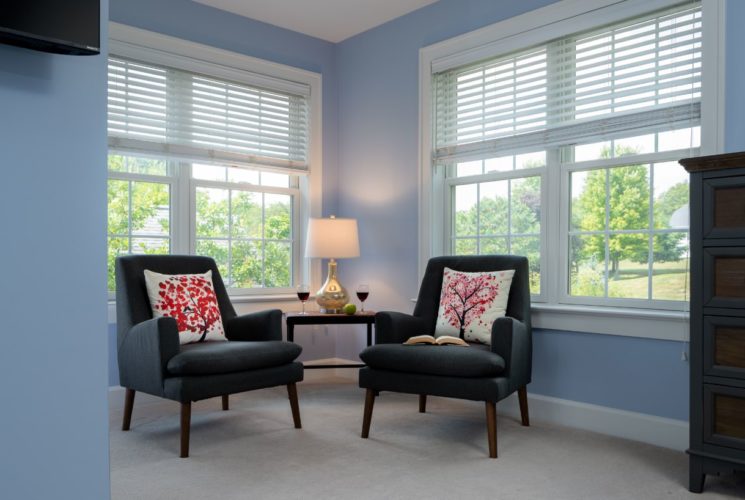 Bedroom sitting area with blue walls, white trim, dark upholstered chairs, wodoen dresser, and multiple windows