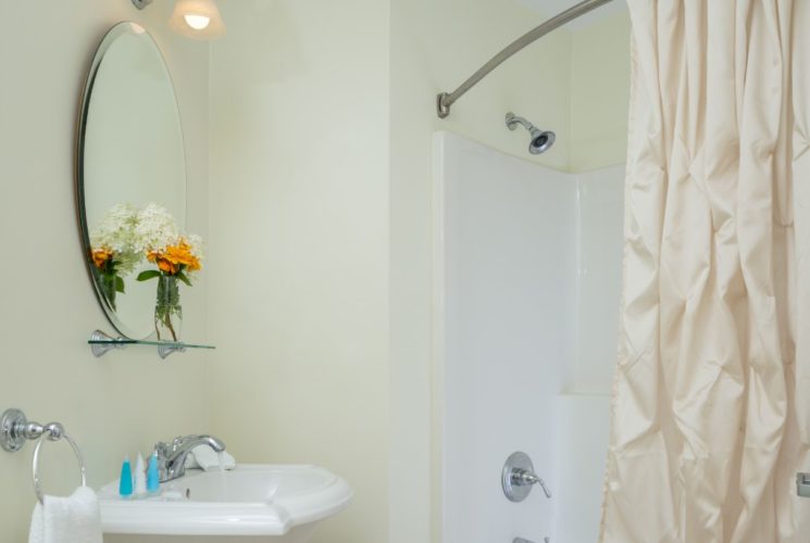 Bathroom with light colored walls, white pedestal sink, oval mirror, and white tub with shower