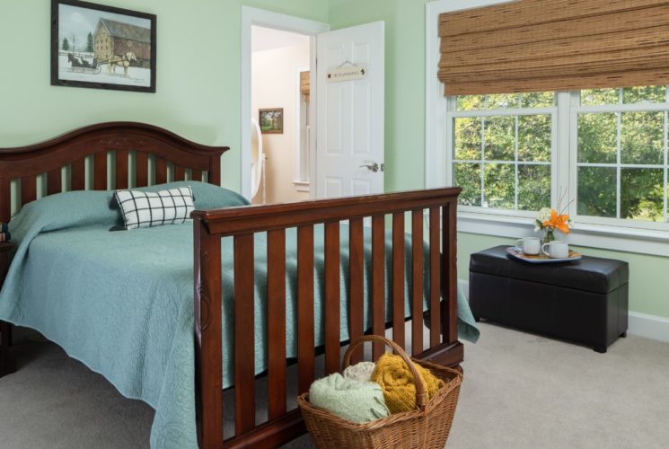 Bedroom with light green walls, carpeting, dark wooden bed, light blue bedding, wooden nightstand, and dark leather trunk