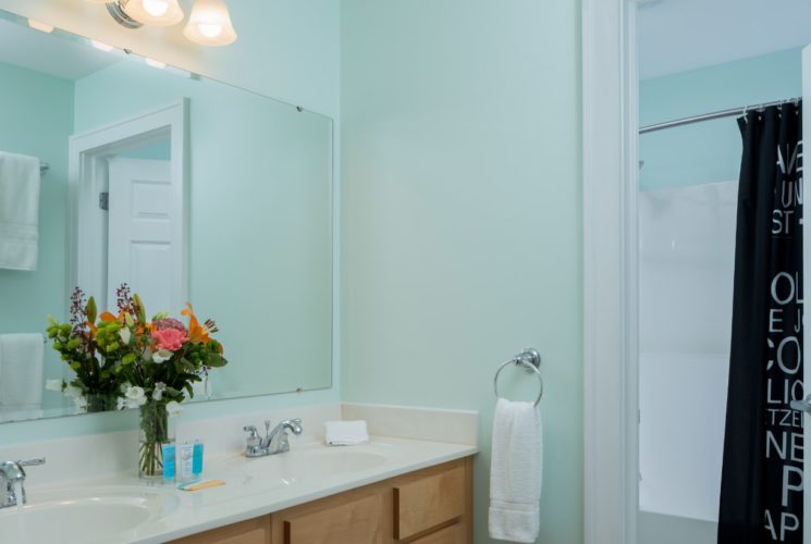 Bathroom with light green walls, white counters, double sinks, wooden vanity, and large mirror