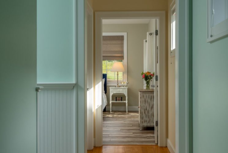 Hallway with light green walls, white trim, and open door into bedroom with light colored walls and hardwood flooring