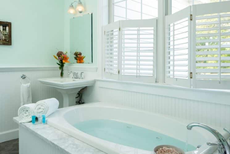 Bathroom with light green walls, white paneling, tile flooring, white vanity, and jetted tub