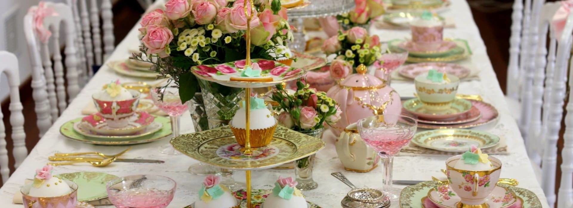 Large table with white tablecloth and multiple placesettings for tea and desserts