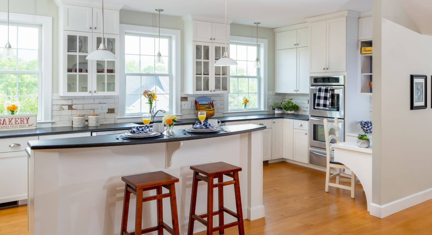 Large kitchen with white cabinets, dark countertop, island, wooden barstools, stainless steel appliances, and multiple windows