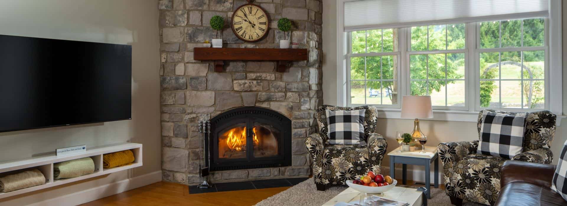 Living room with light colored walls, hardwood flooring, stone brick fireplace, leather sofa, upholstered chairs, and large wall-mounted TV